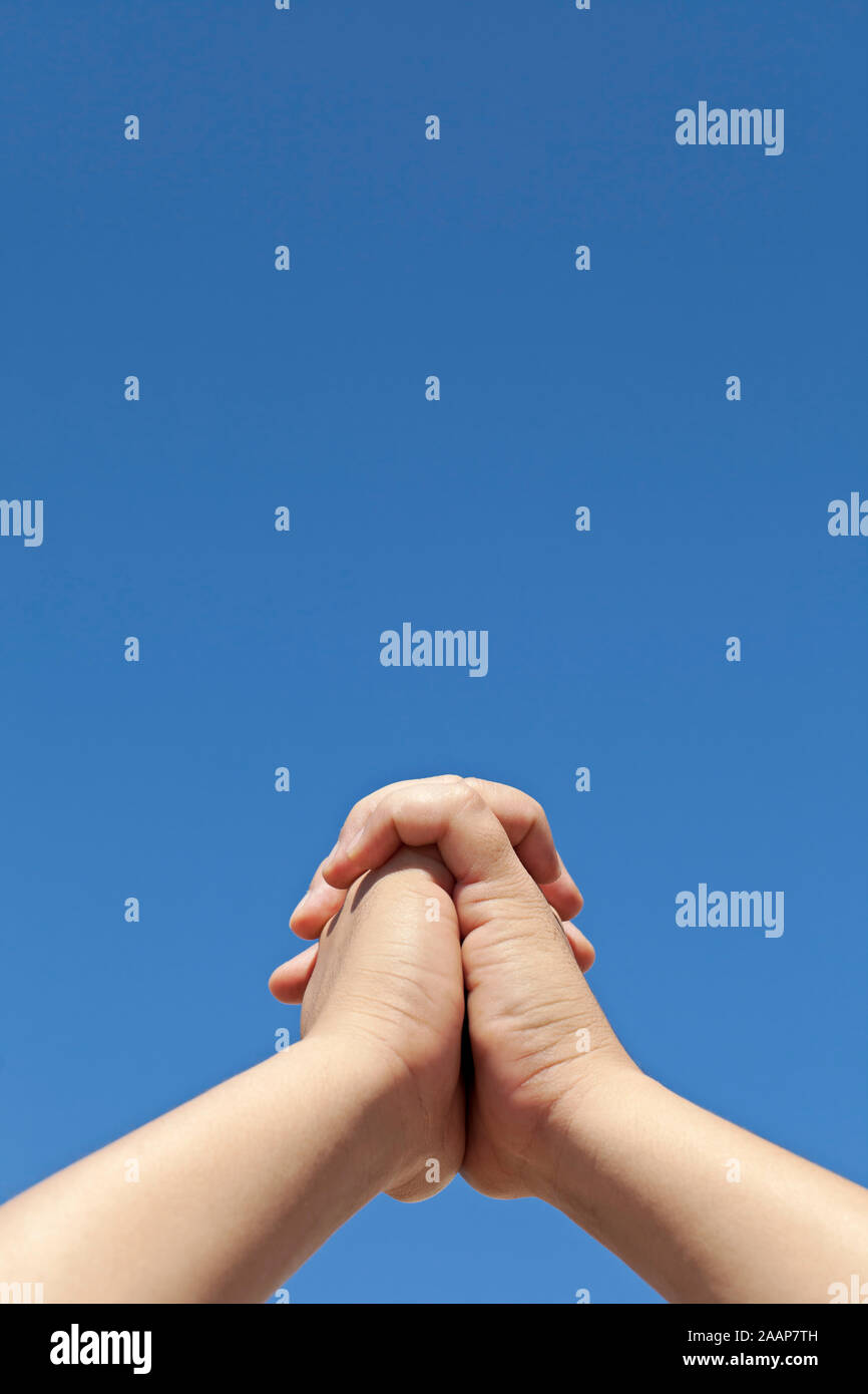 Jeune homme sensibilisation plié mains contre un ciel bleu Banque D'Images