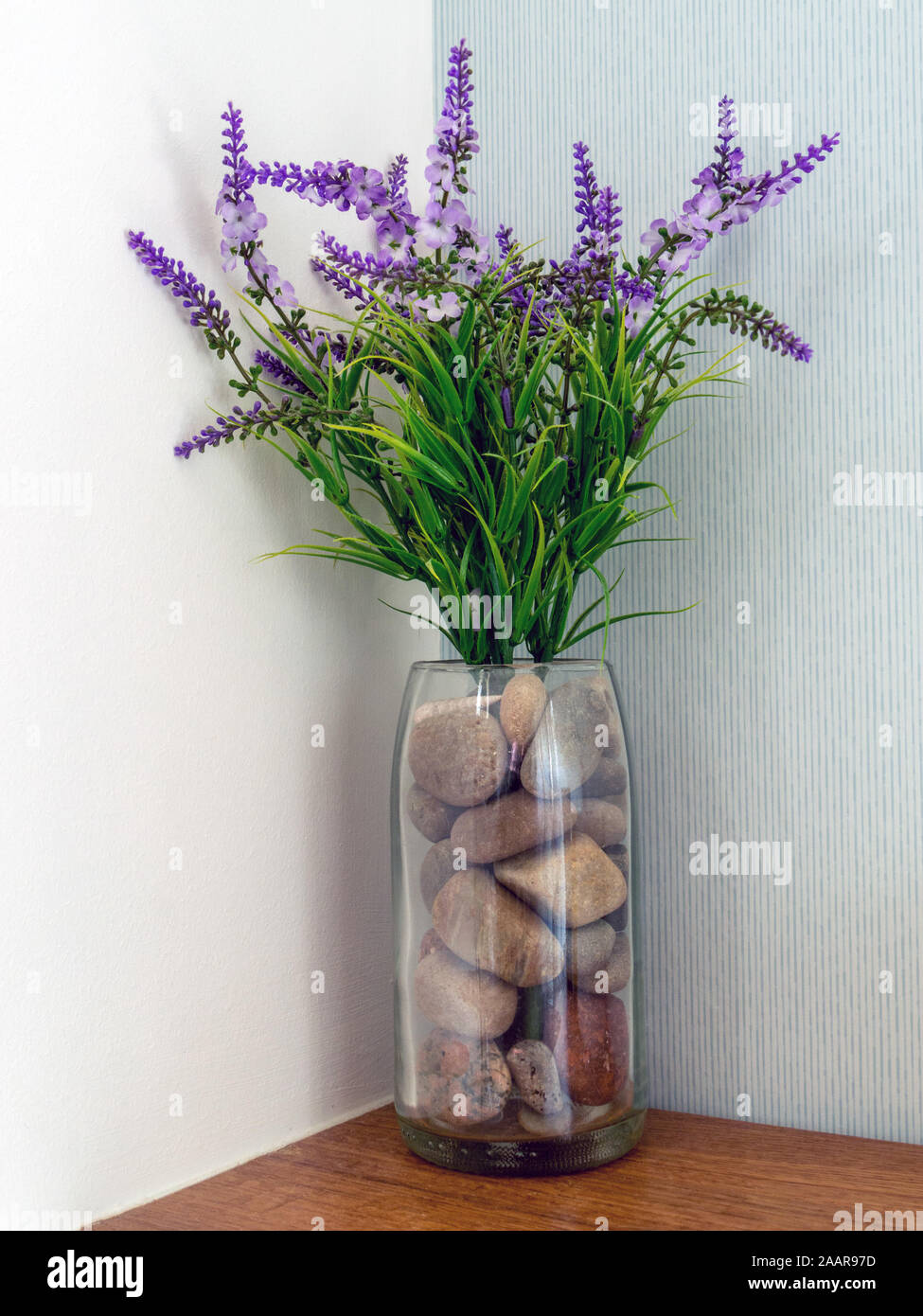 Simple et attrayant de l'arrangement de fleurs artificielles fleurs lavandes violets et des cailloux dans un vase de verre. Banque D'Images