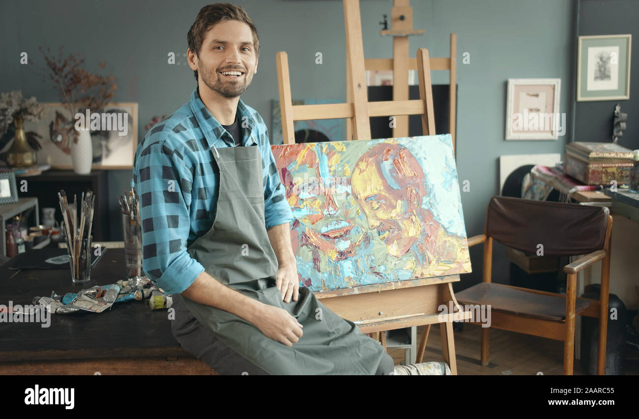 Portrait de jeune homme assis peintre heureux sur fond de sa nouvelle peinture Banque D'Images
