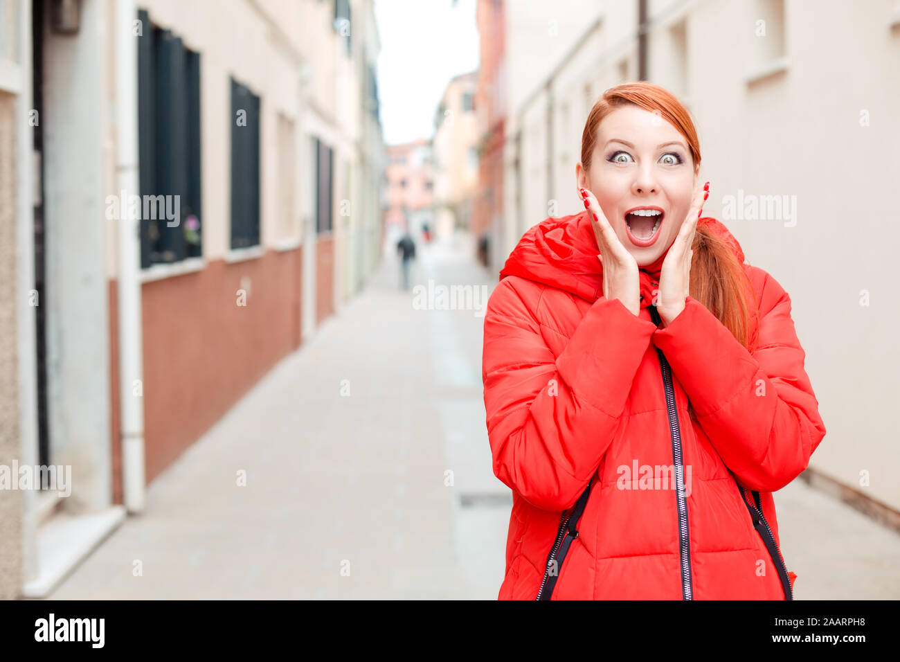 Traiter ou vendre, nouvelle choquante. Femme choqué à Murano, Venise, Italie. Modèle irlandais en manteau d'hiver rouge vêtements, cheveux roux standing on urban backgroun Banque D'Images