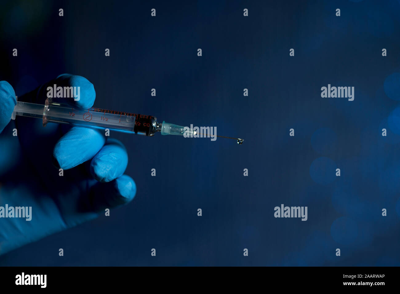 Aiguille hypodermique avec détenus par des gouttelettes main gantée sur bleu foncé. Banque D'Images