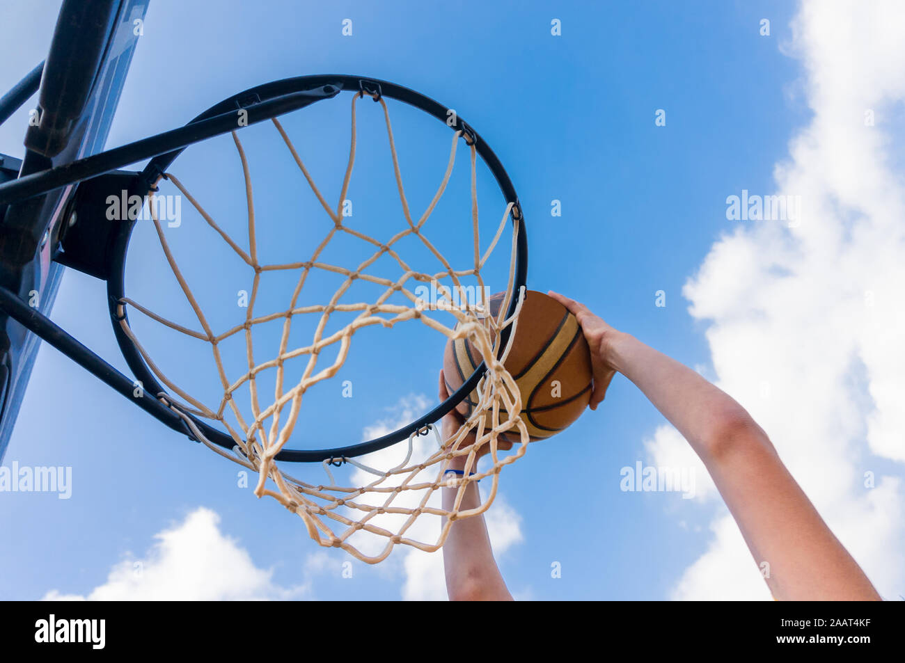 Jeune garçon faisant un slam dunk au basket-ball de rue avec ciel bleu et nuages blancs Banque D'Images