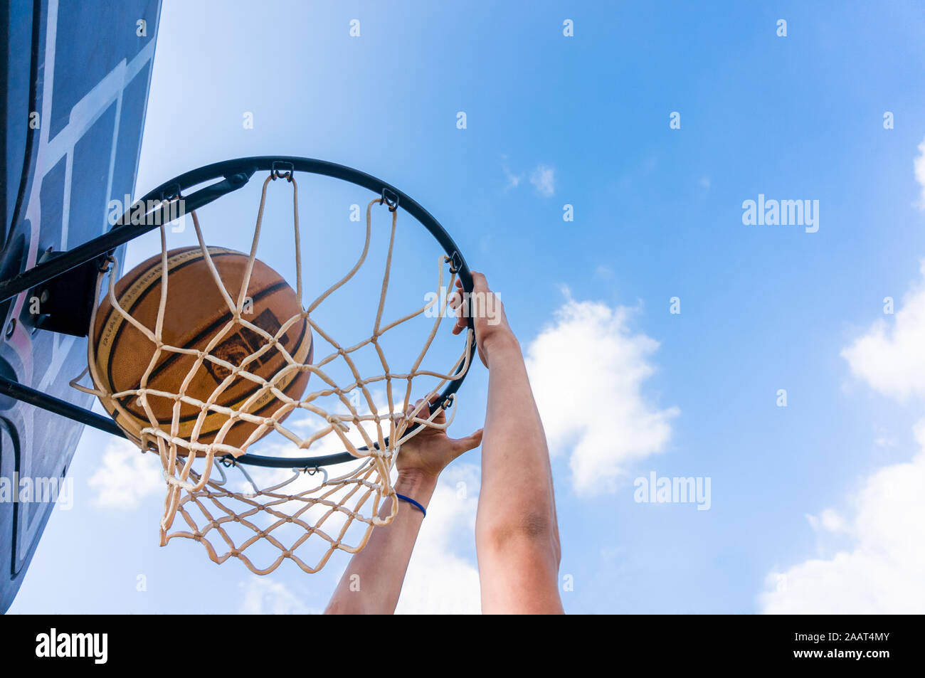 Jeune garçon faisant un slam dunk au basket-ball de rue avec ciel bleu et nuages blancs Banque D'Images
