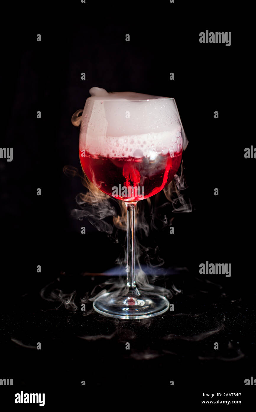 Une tasse de cocktail rouge avec de la glace sèche et fumée fond noir Banque D'Images
