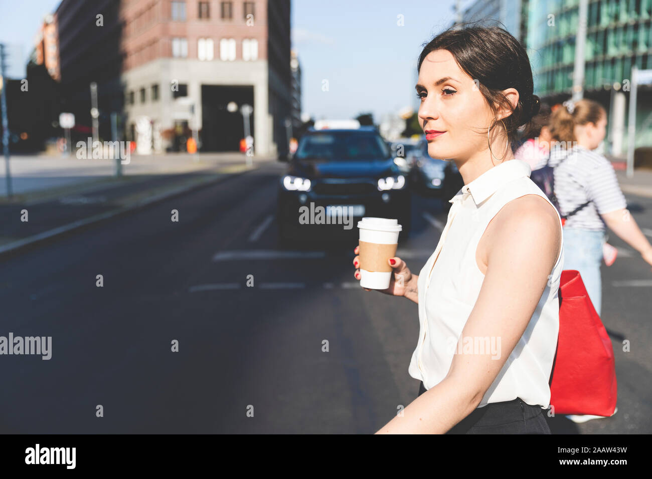 Young businesswoman avec café à emporter de traverser la rue dans la ville, Berlin, Allemagne Banque D'Images