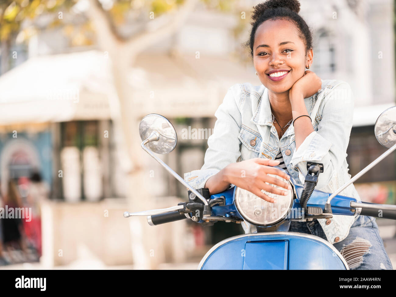 Portrait of happy young woman with motor scooter dans la ville, Lisbonne, Portugal Banque D'Images