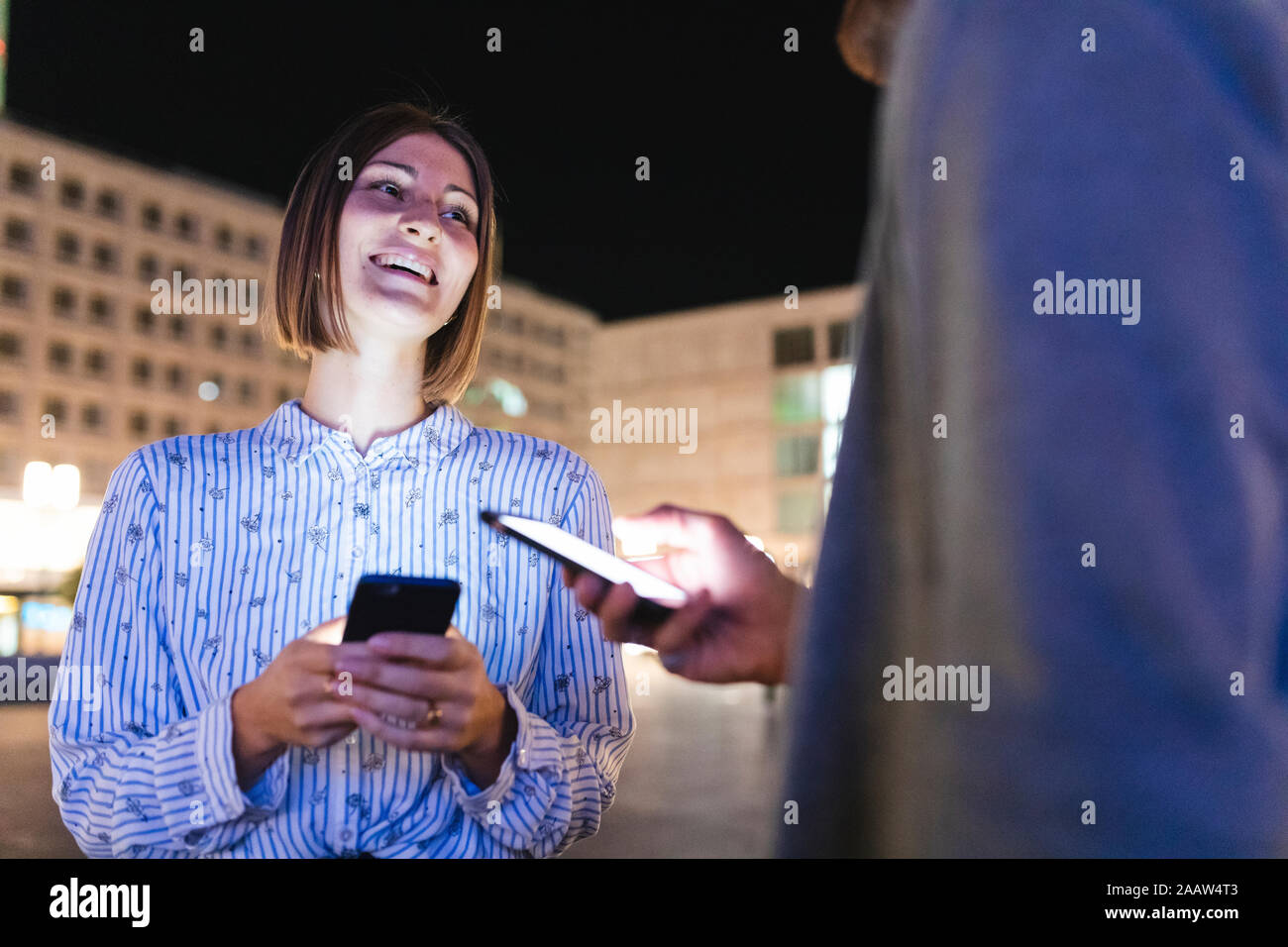 Couple heureux dans la ville la nuit contrôle sur leurs téléphones, Berlin, Allemagne Banque D'Images