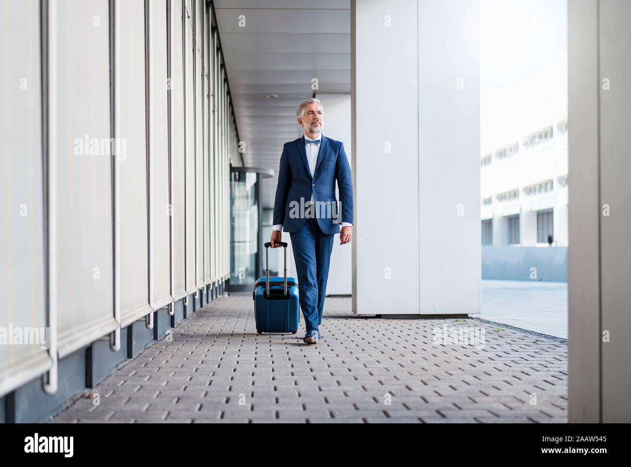 Mature businessman dans une zone de passage avec valise roulant sur le rendez-vous Banque D'Images