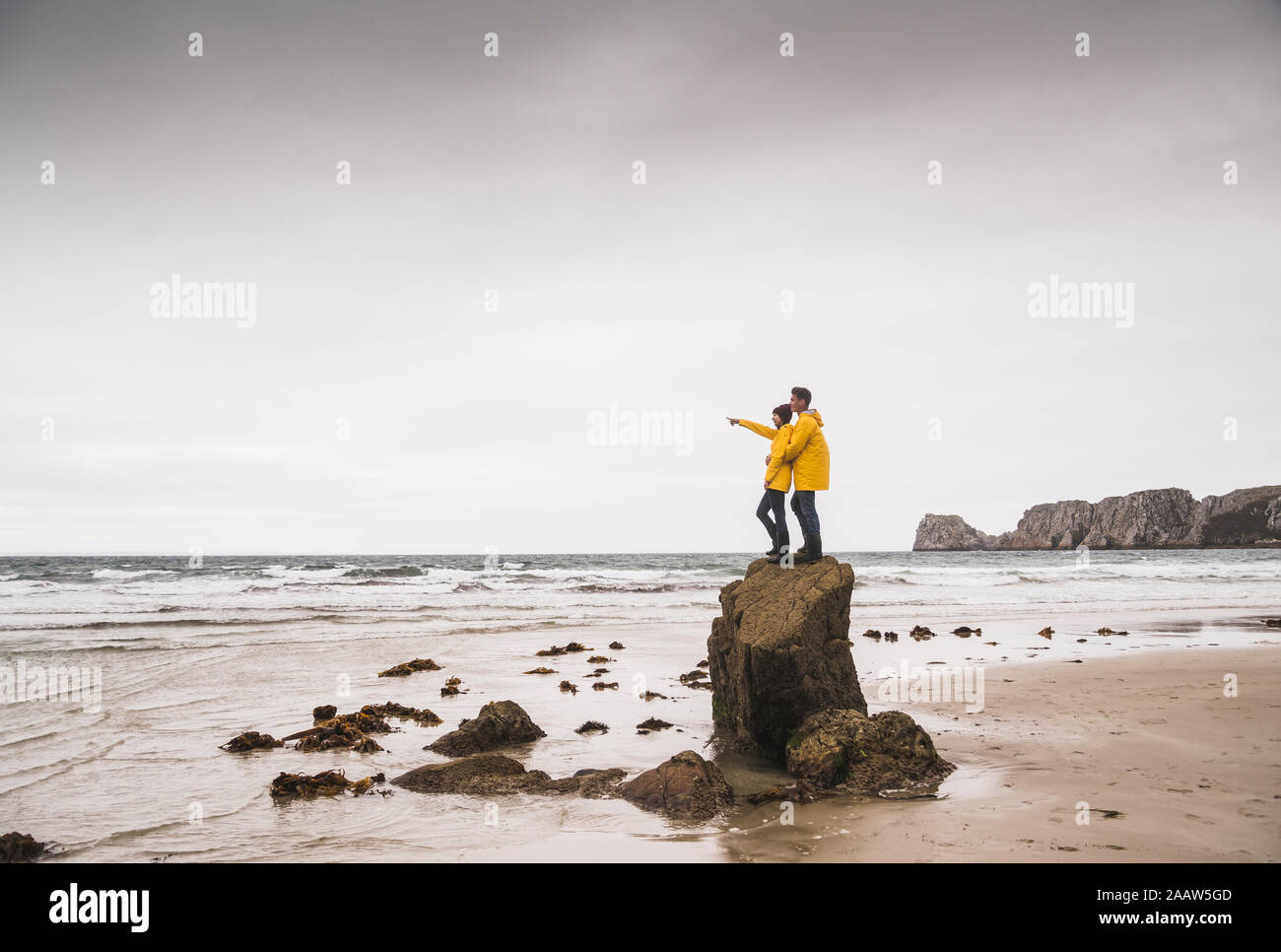 Jeune femme portant des vestes de pluie jaune et l'article sur rock à la plage, Bretagne, France Banque D'Images