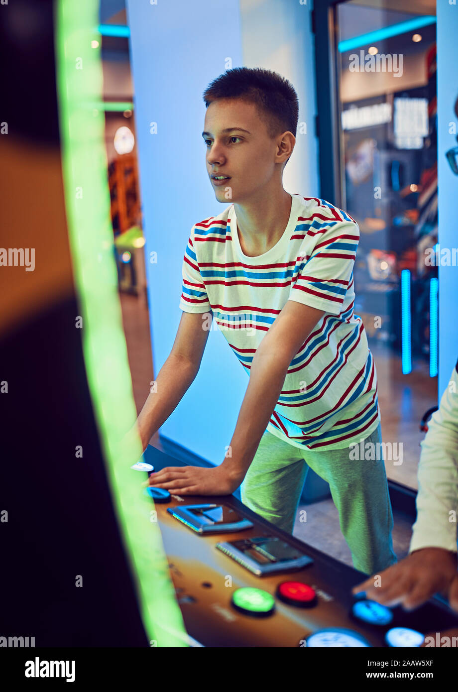 Teenage boy à jouer avec un appareil de jeu dans une salle de jeux électroniques Banque D'Images