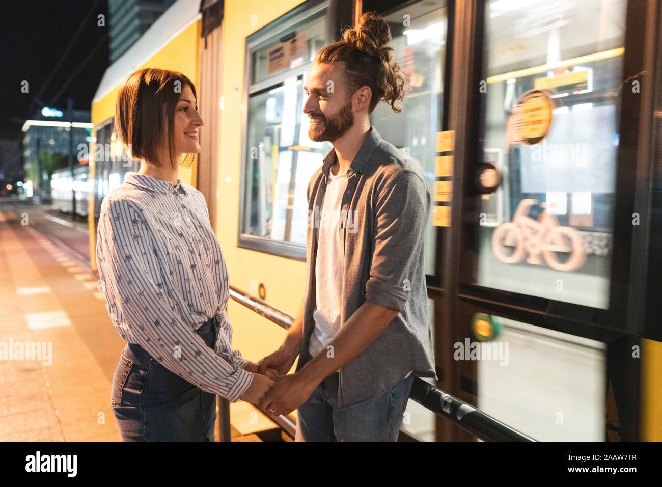 Smiling couple holding hands and à l'autre avec un tram à l'arrière-plan, Berlin, Allemagne Banque D'Images