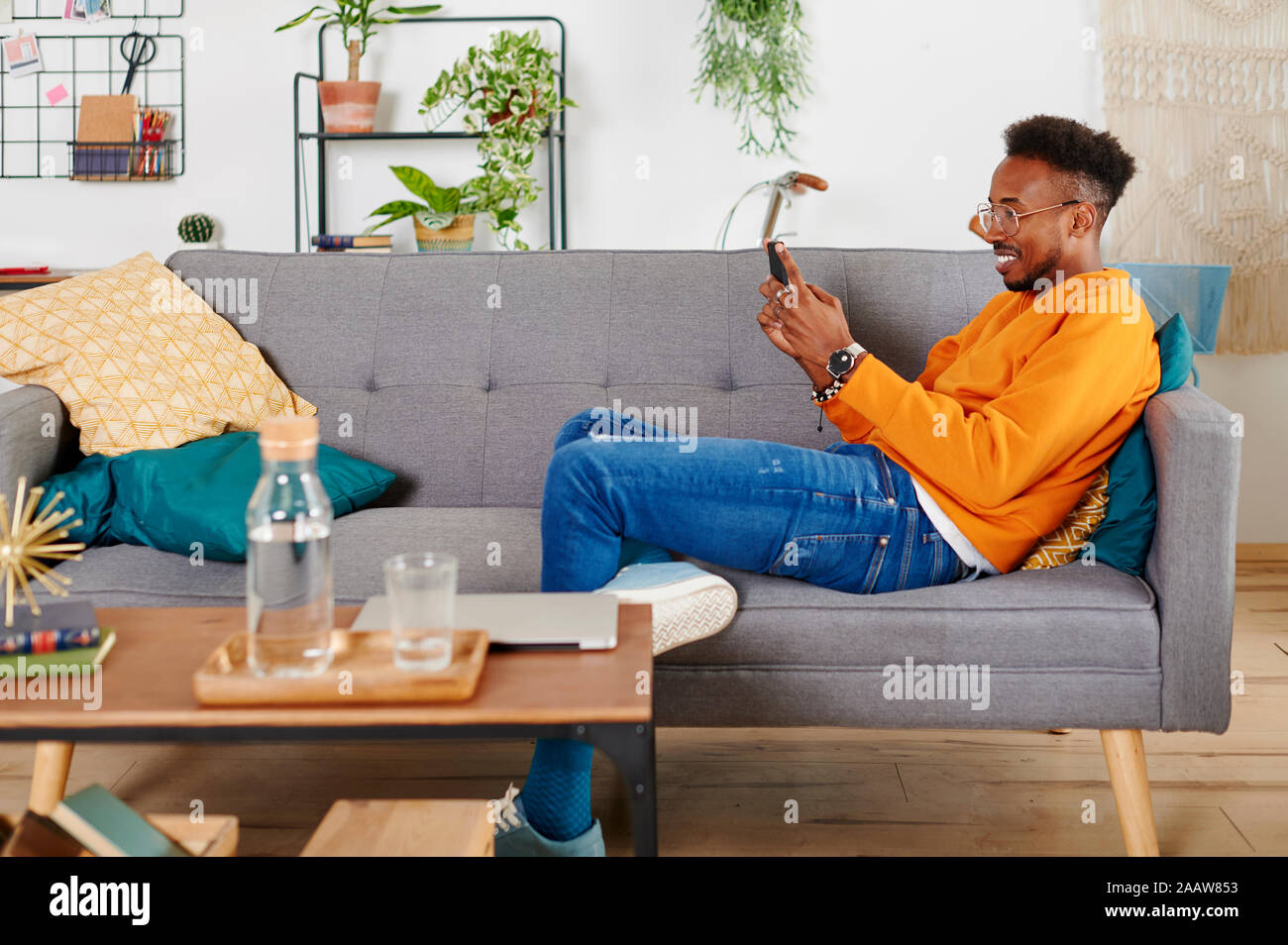 Young smiling man sitting on a couch et using smartphone Banque D'Images