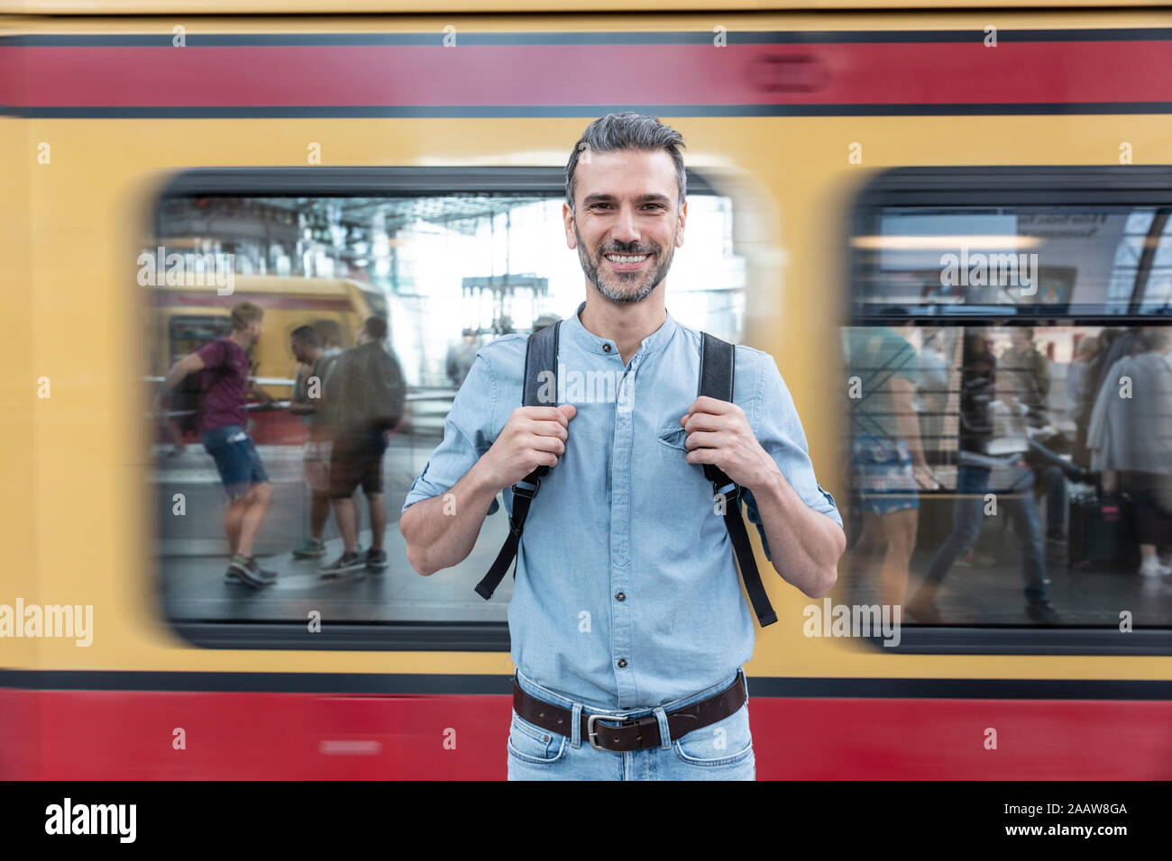 Portrait d'homme souriant à la plate-forme de la gare avec train en arrière-plan, Berlin, Allemagne Banque D'Images