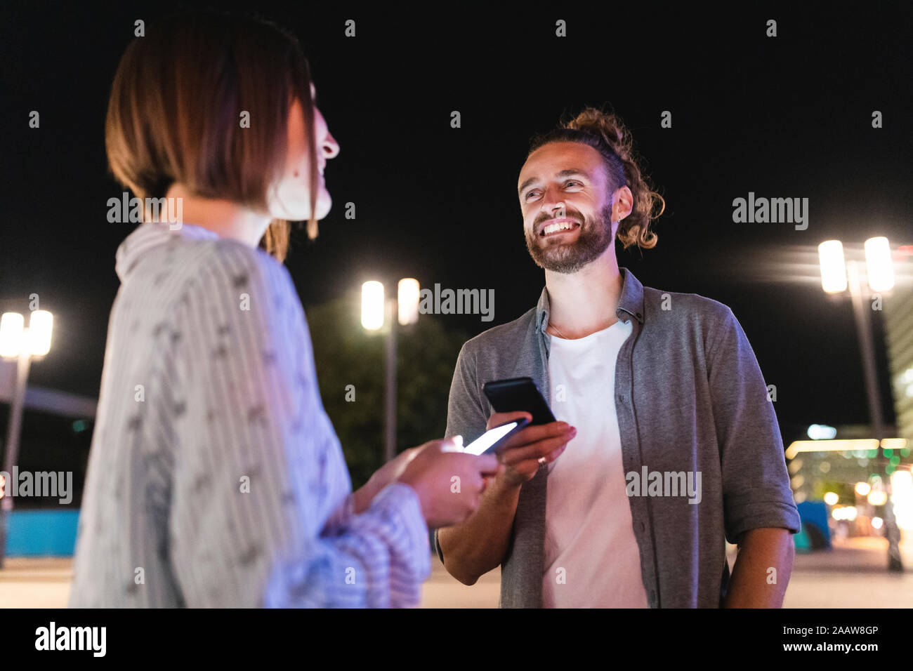 Couple heureux dans la ville la nuit contrôle sur leurs téléphones, Berlin, Allemagne Banque D'Images