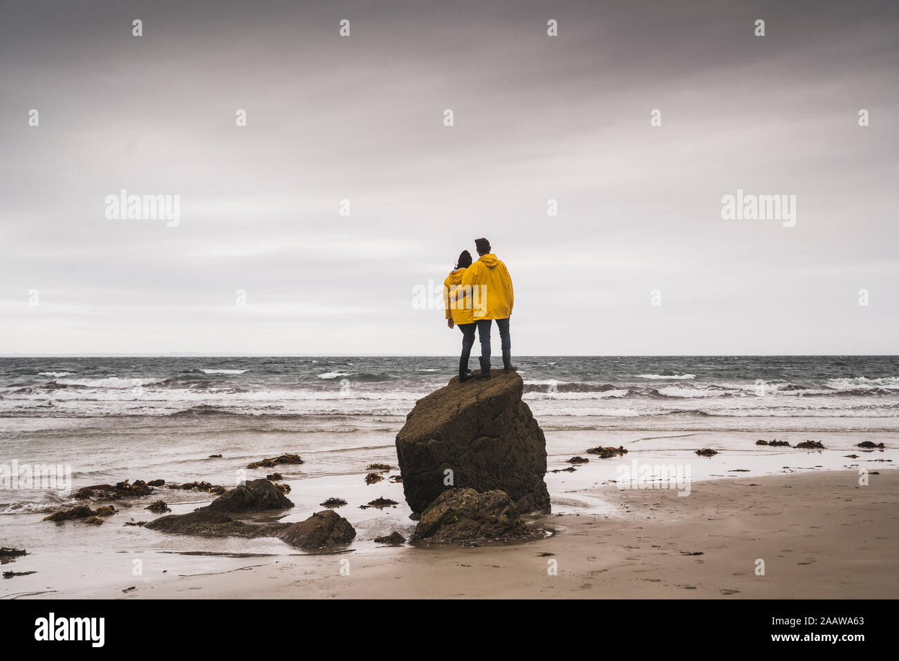 Jeune femme portant des vestes de pluie jaune et l'article sur rock à la plage, Bretagne, France Banque D'Images