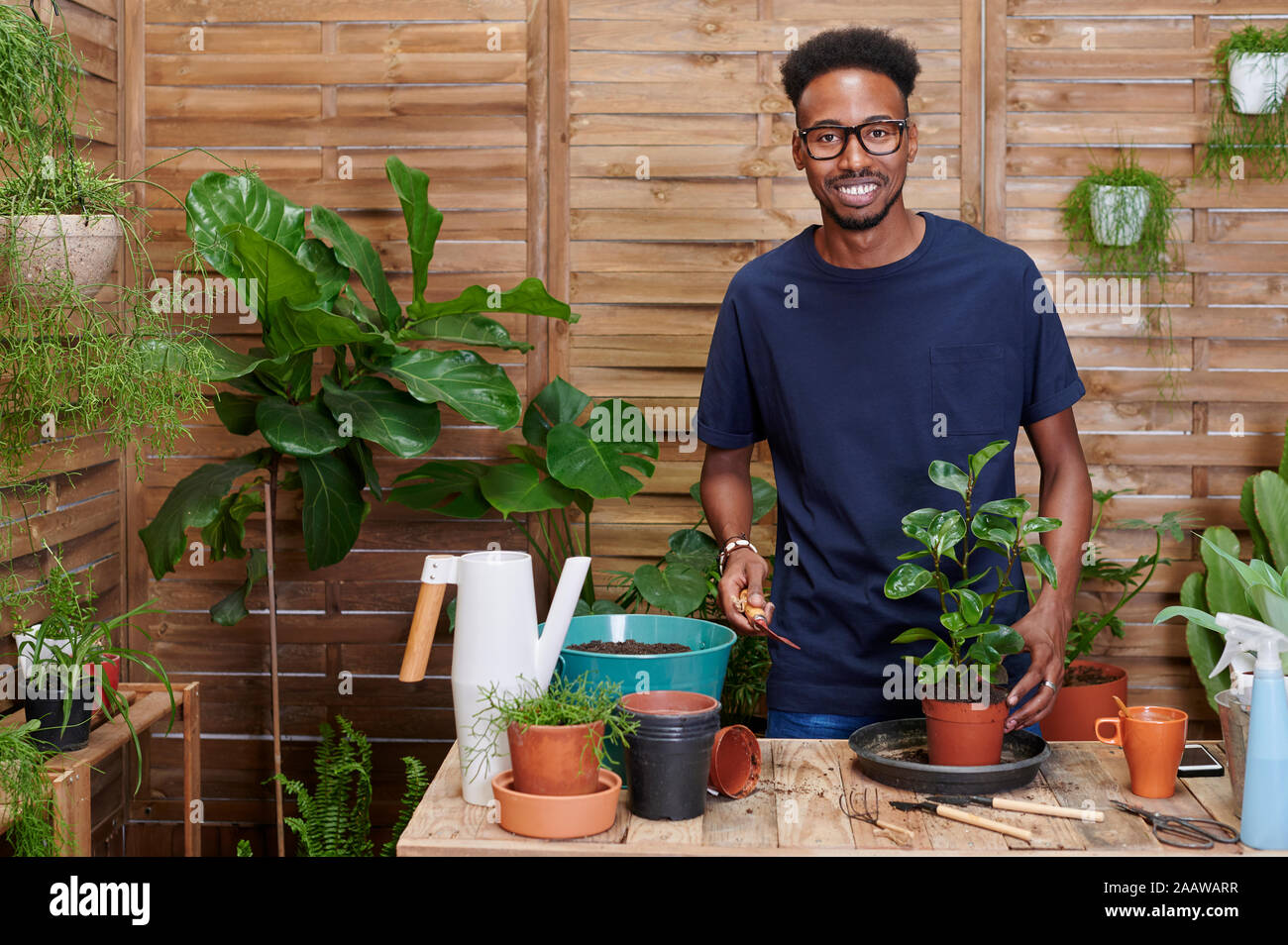 Portrait of a smiling young man rempotage une plante sur sa terrasse Banque D'Images