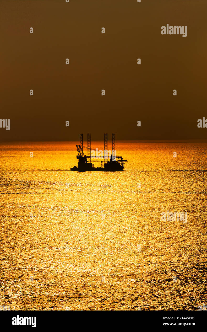 L'installation d'éoliennes offshore bateau naviguant au large dans la mer pendant le coucher du soleil, de la côte ouest, Ecosse, Royaume-Uni Banque D'Images