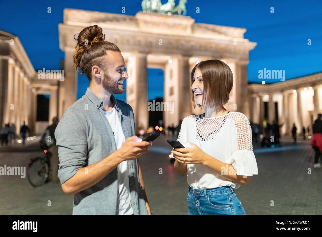 Heureux couple using smartphones à porte de Brandebourg à l'heure bleue, Berlin, Allemagne Banque D'Images