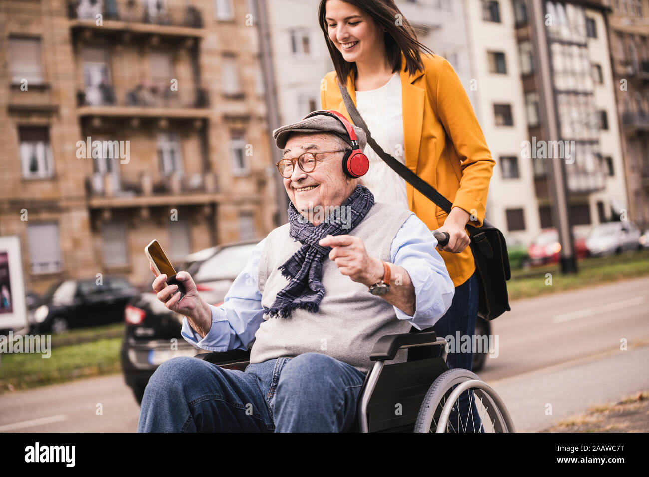 Laughing young woman happy senior man with headphones et smartphone en fauteuil roulant Banque D'Images