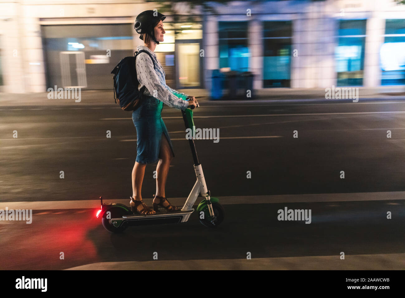 Jeune femme équitation un scooter électrique dans la ville de nuit, Berlin, Allemagne Banque D'Images