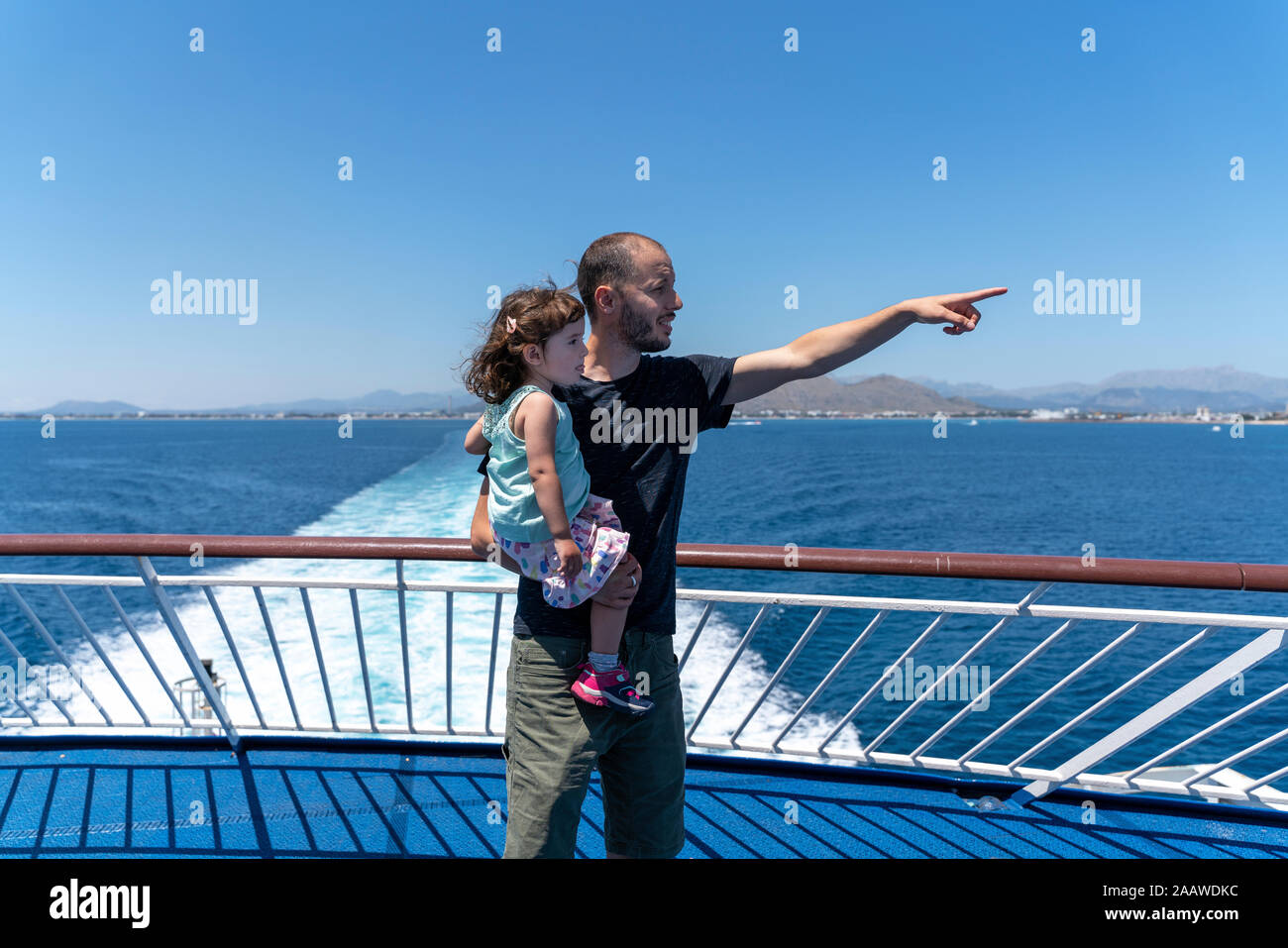 Père debout sur le pont d'un navire avec petite fille sur son bras pointant à distance, Mallorca, Espagne Banque D'Images