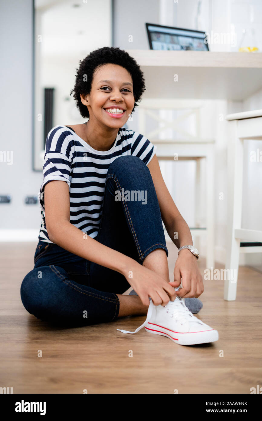 Portrait de jeune femme assise sur le sol à ses baskets de laçage Banque D'Images