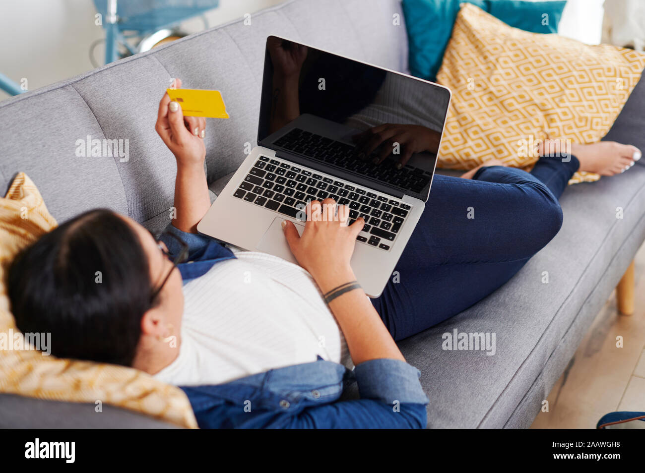 Young woman using laptop et allongé sur un canapé Banque D'Images