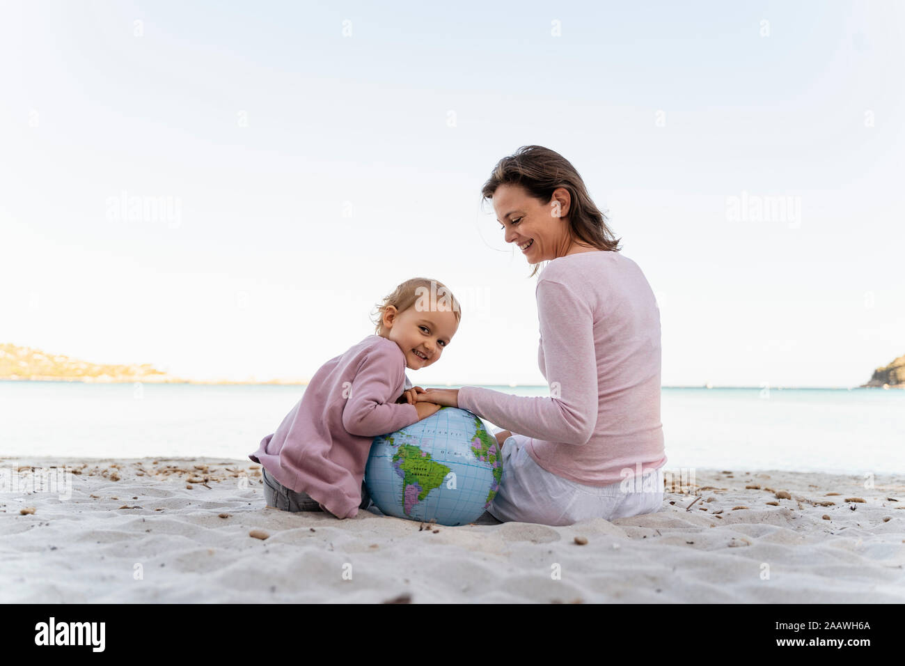 Portrait of happy petite fille assise avec sa mère sur la plage jouer avec ballon de plage de la Terre Banque D'Images