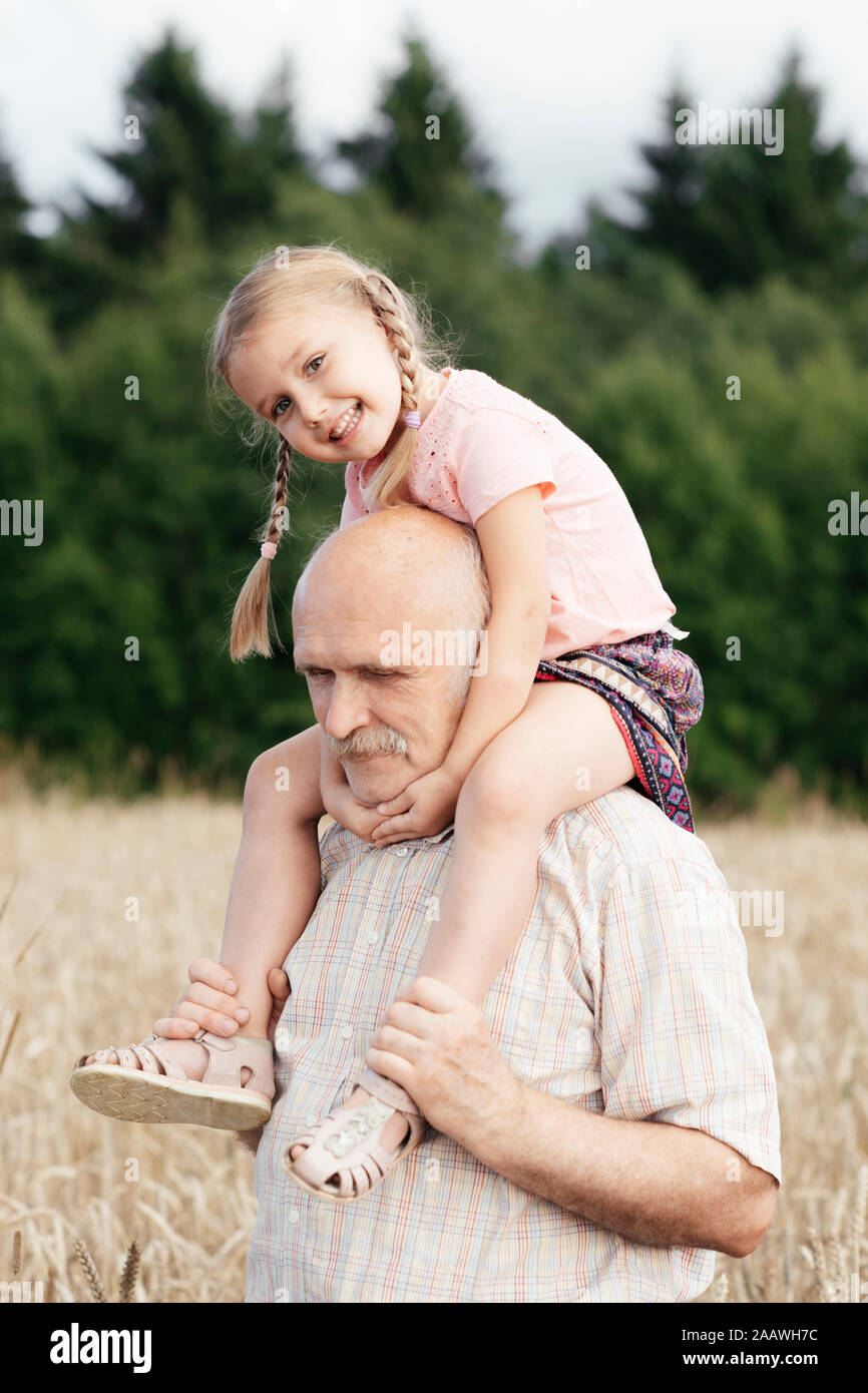 Portrait of happy little girl sur les épaules de grand-père dans un champ d'avoine Banque D'Images