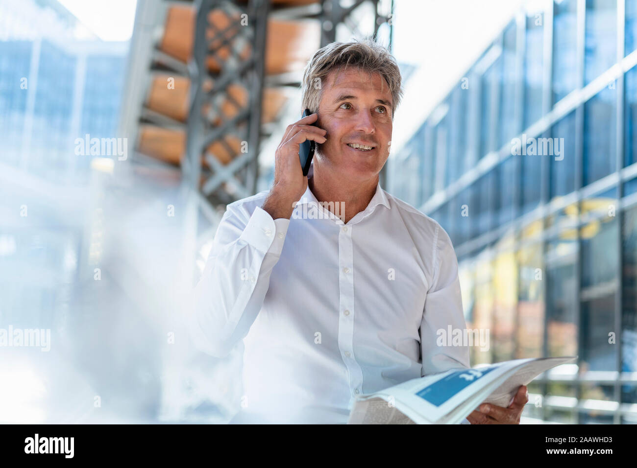 Homme d'âge mûr avec du papier journal sur le téléphone dans la ville Banque D'Images