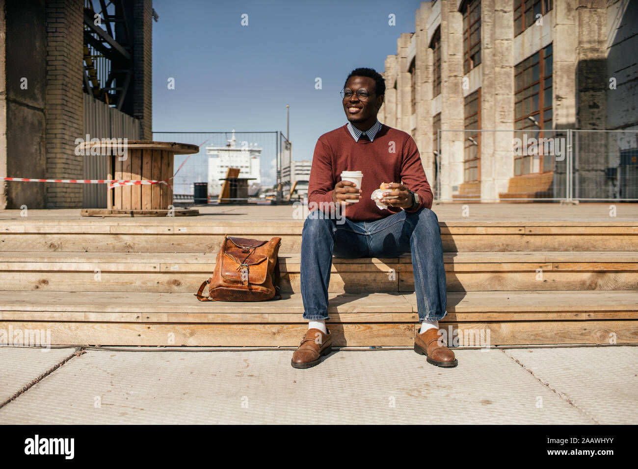 Jeune homme assis sur les marches dans la ville, manger des hamburgers, de boire du café Banque D'Images