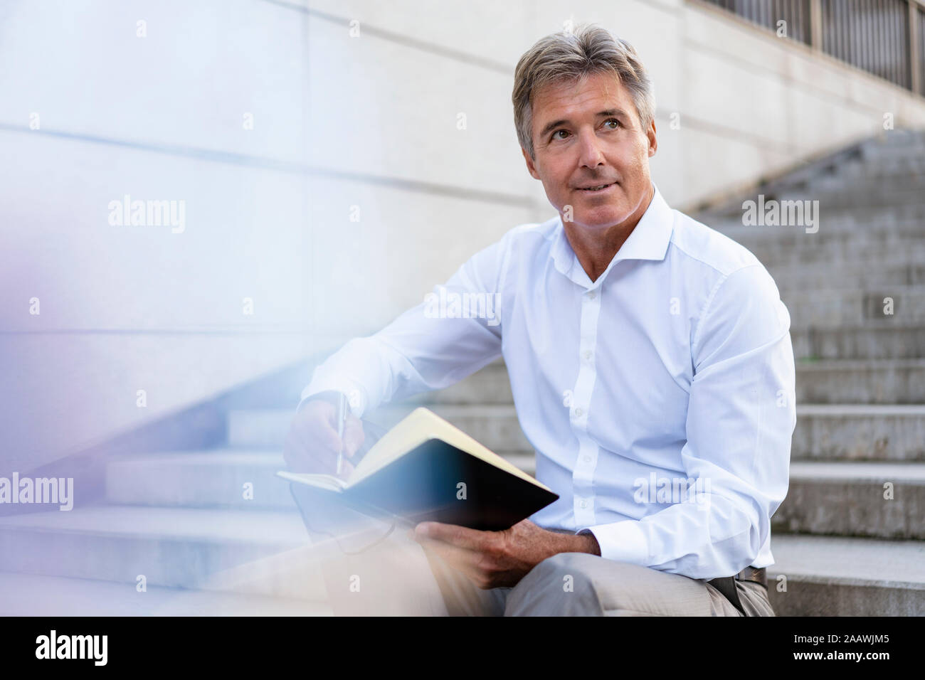 Mature businessman sitting on stairs with notebook Banque D'Images