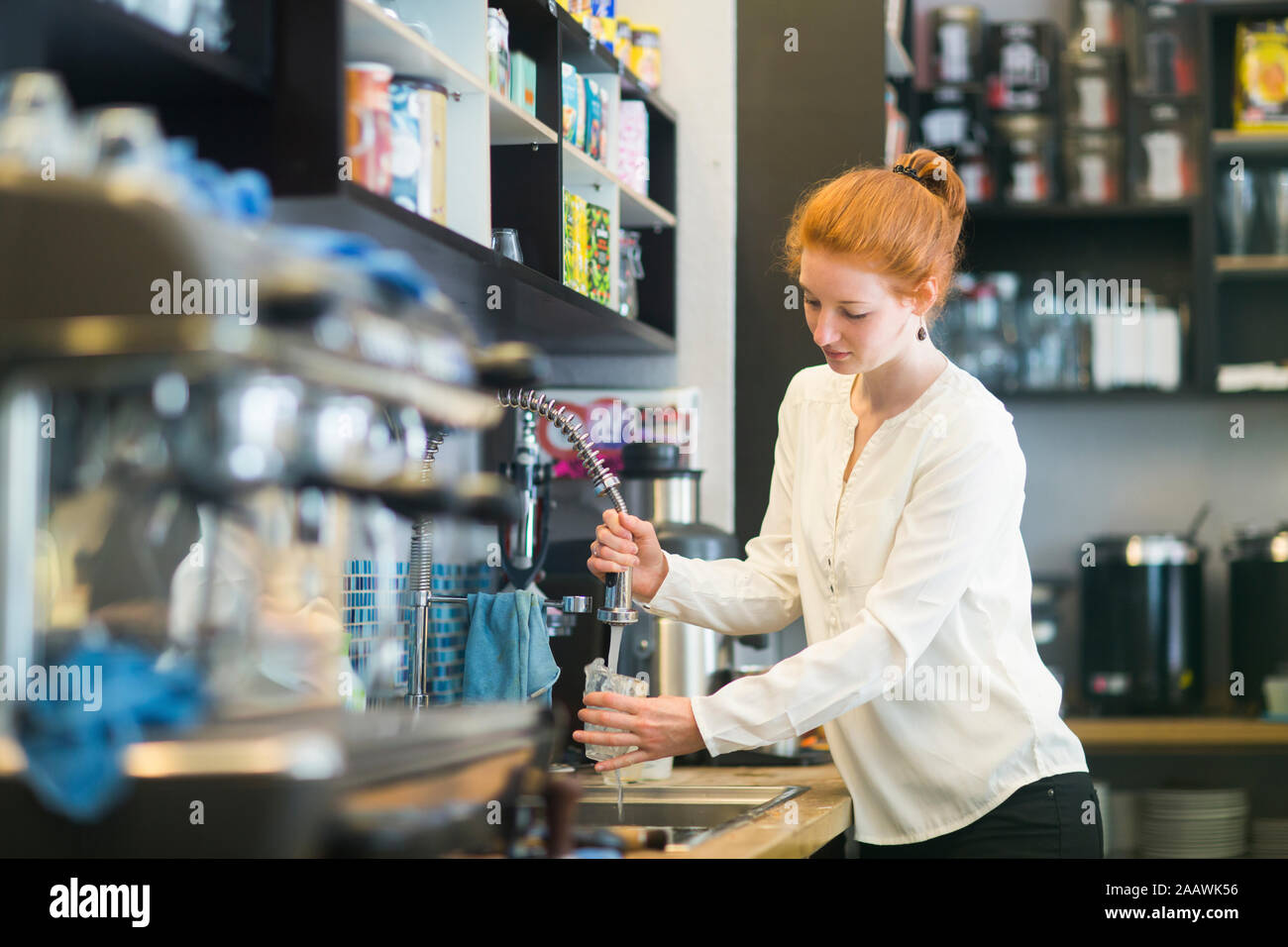 Jeune femme travaillant dans un café, lave-vaisselle Banque D'Images