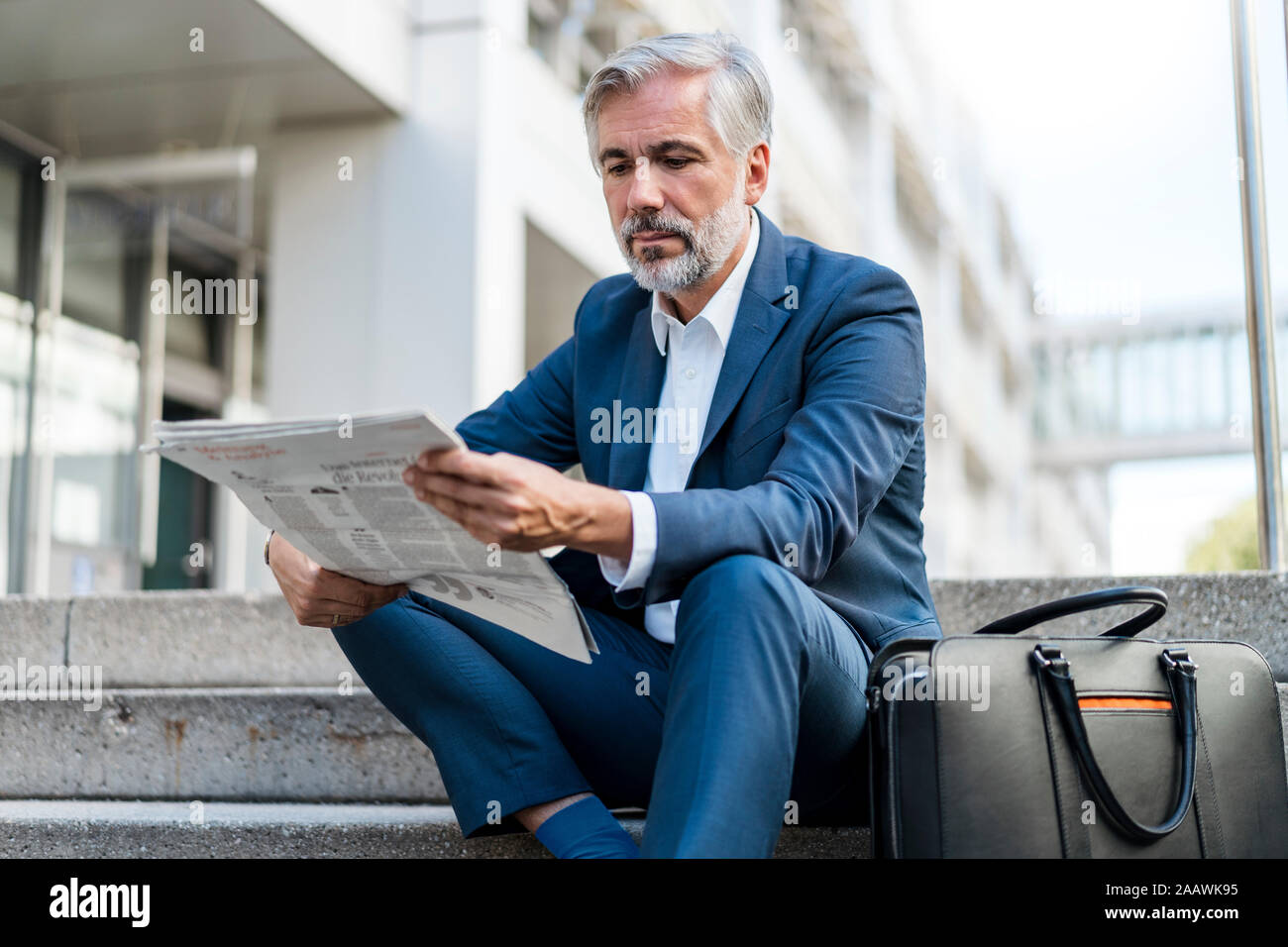 Mature businessman sitting on stairs dans la ville reading newspaper Banque D'Images