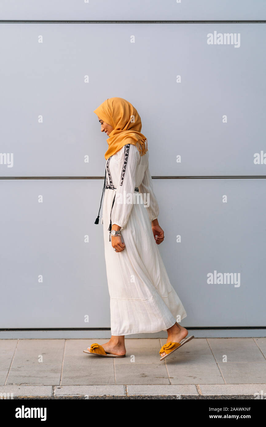 Jeune femme musulmane portant le hijab et jaune marchant devant un mur blanc Banque D'Images