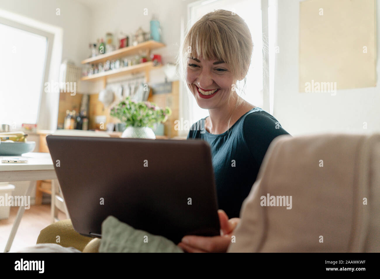 Portrait of happy woman sitting in the kitchen using laptop Banque D'Images