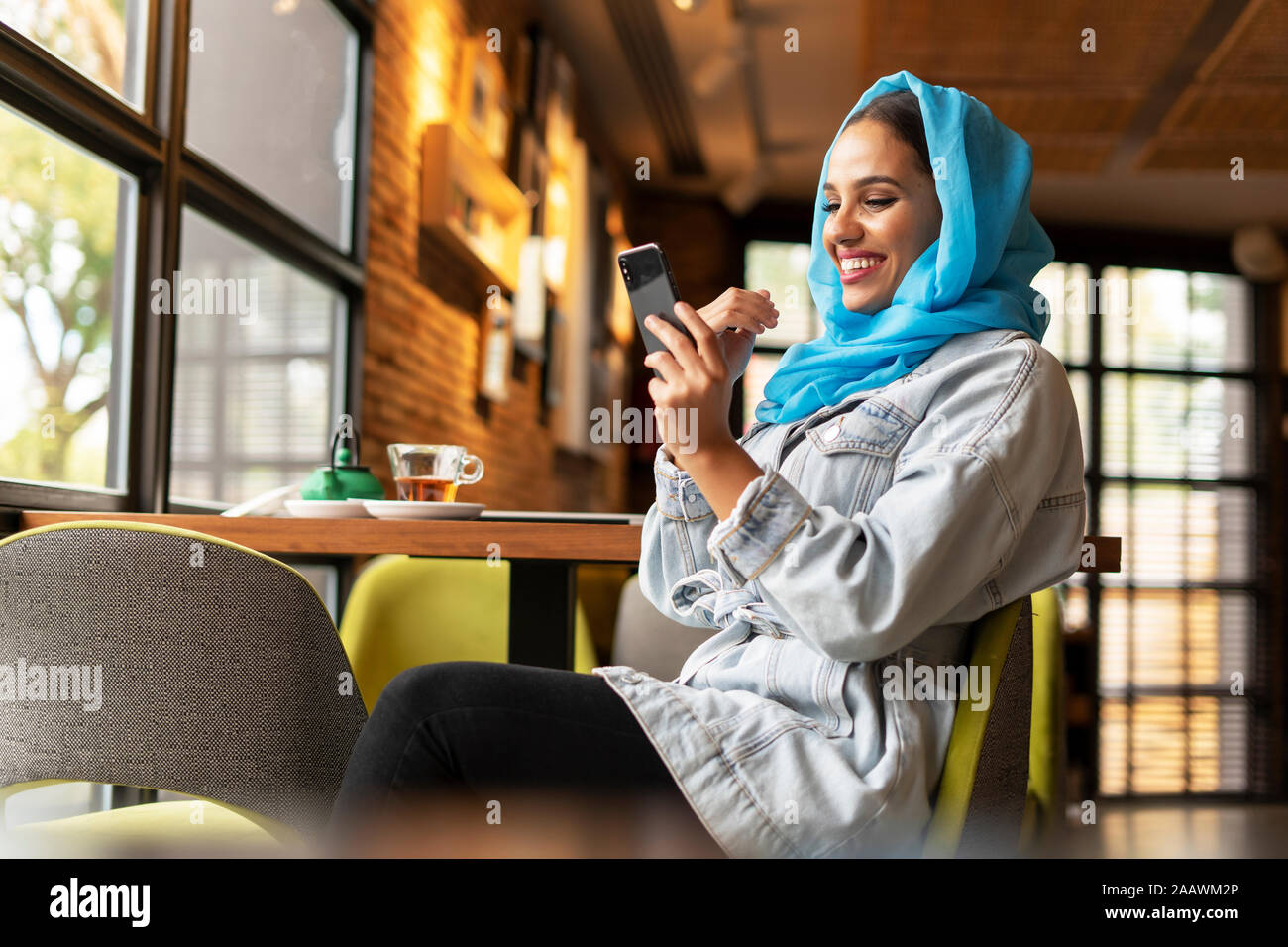 Jeune femme portant le hijab et turquoise using smartphone in a cafe Banque D'Images