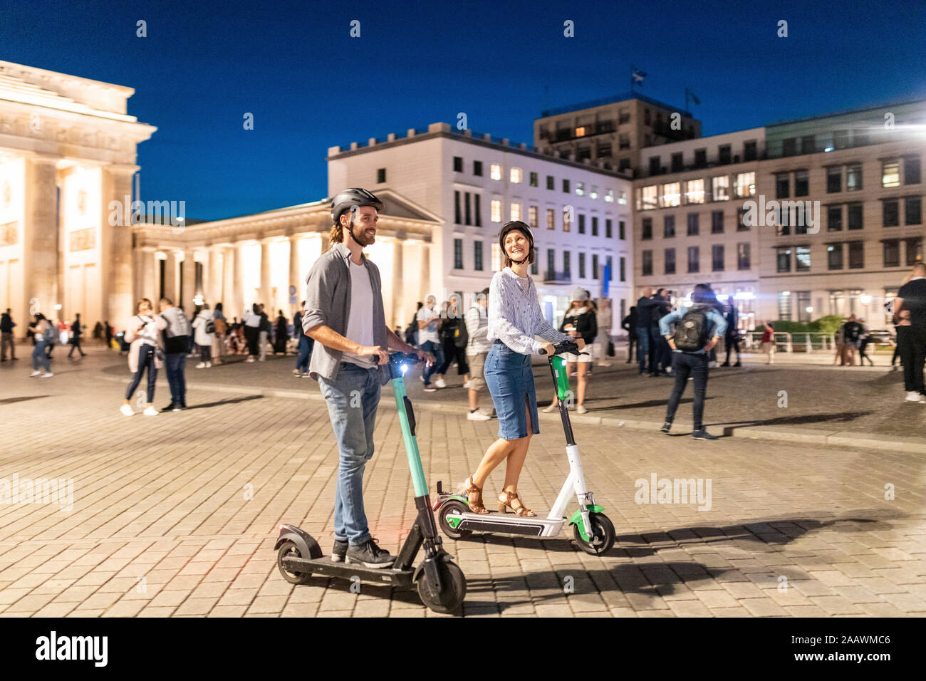 Jeune couple avec des scooters électriques à la porte de Brandebourg la nuit, Berlin, Allemagne Banque D'Images