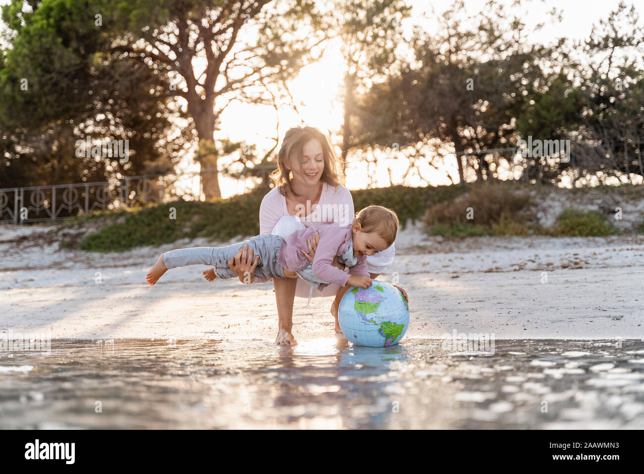 Mère et fille jouer ensemble avec la terre de ballons de plage à mer Banque D'Images