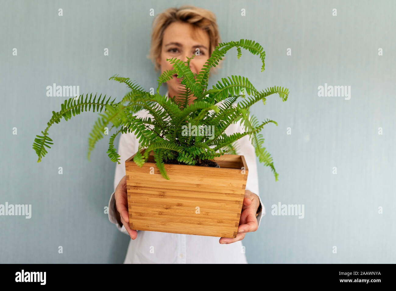 Mature Woman standing à un mur tenant une plante de fougère Banque D'Images