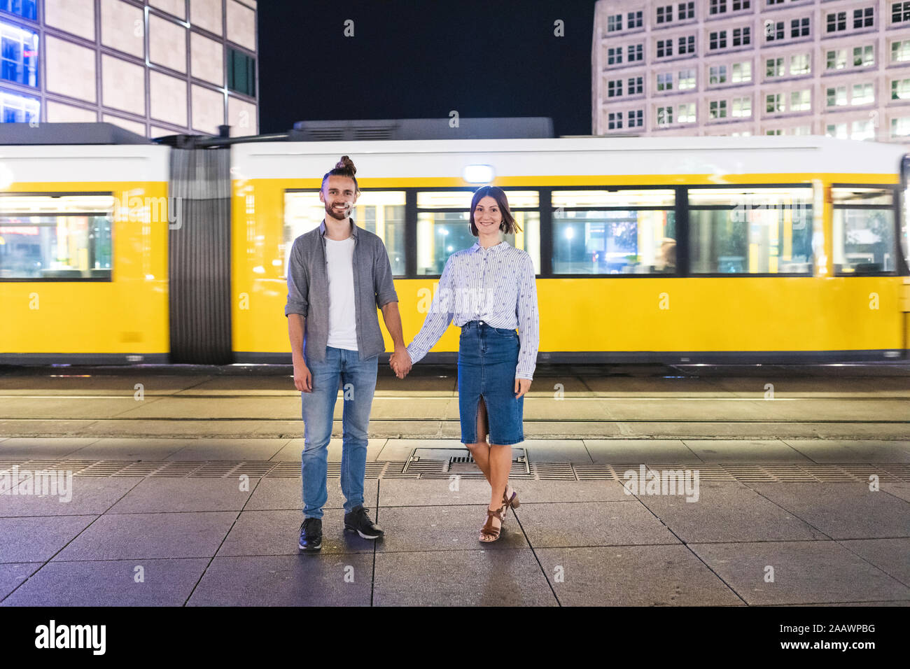 Heureux couple holding hands and looking at camera with tramway sur l'arrière-plan, Berlin, Allemagne Banque D'Images