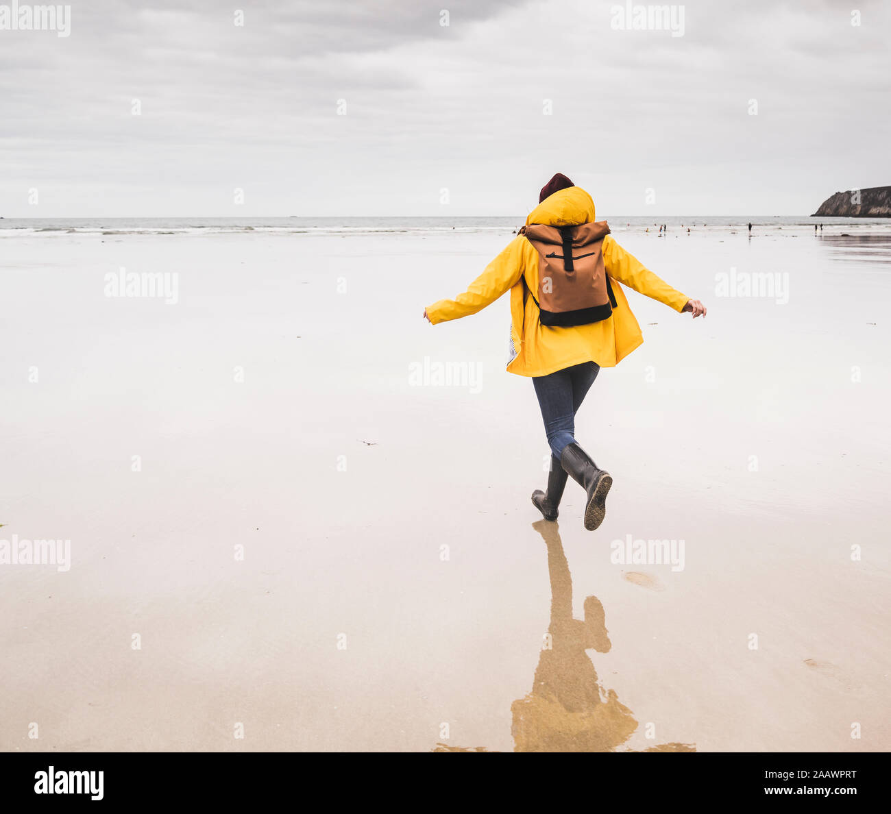 Jeune femme portant veste de pluie jaune et tournant à la plage, Bretagne, France Banque D'Images