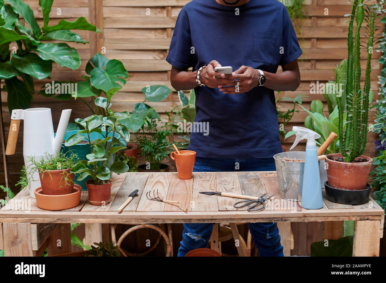 Jeune homme à l'aide du smartphone sur sa terrasse tout en faisant du jardinage Banque D'Images