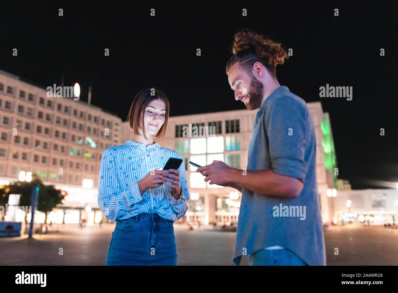 Couple heureux dans la ville la nuit contrôle sur leurs téléphones, Berlin, Allemagne Banque D'Images