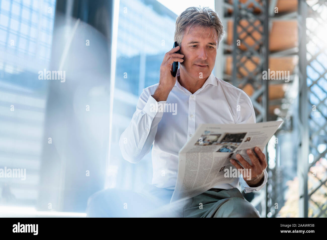 Homme d'âge mûr avec du papier journal sur le téléphone dans la ville Banque D'Images