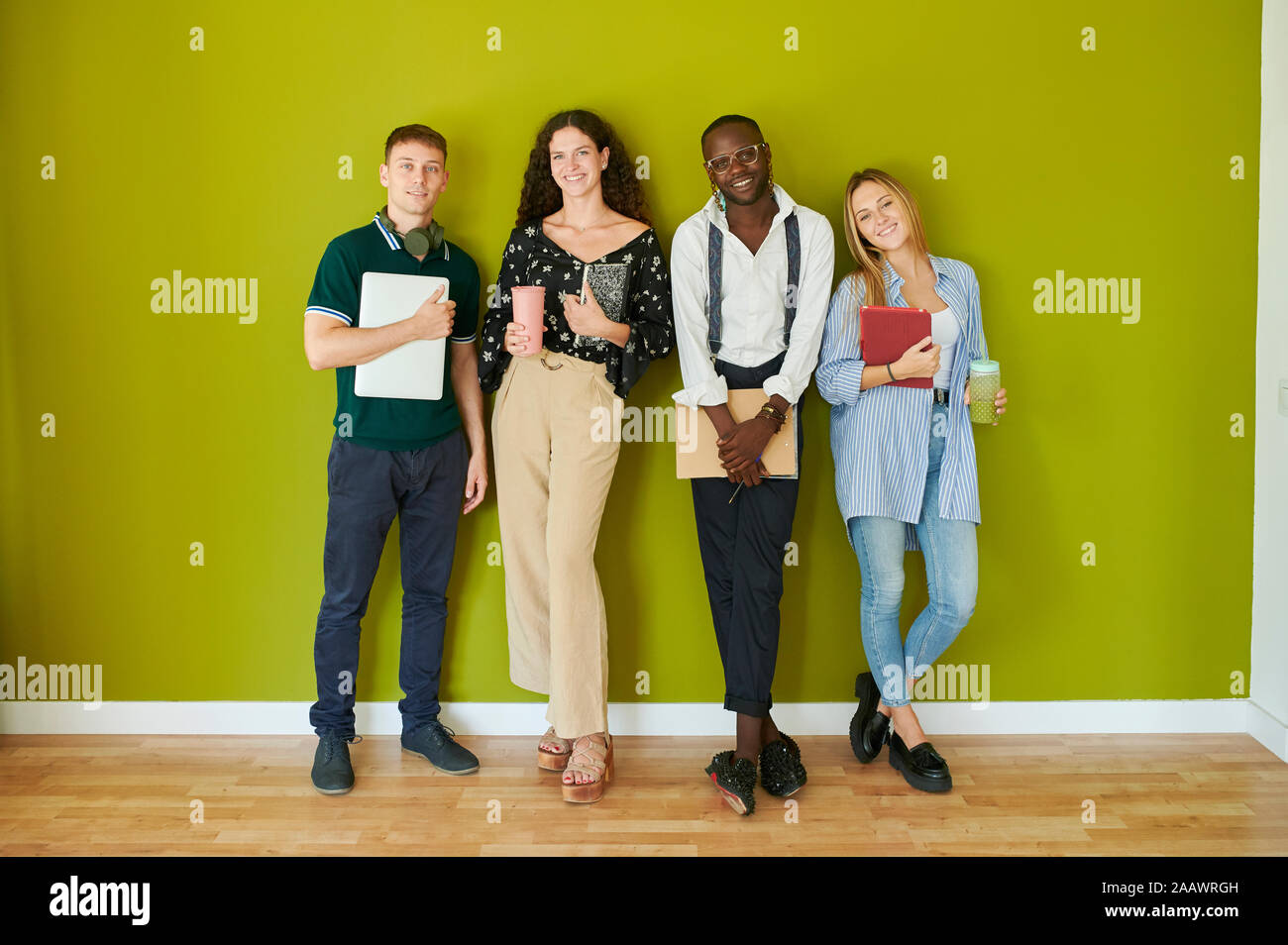 Portrait of smiling casual collègues debout ensemble en face d'un mur vert dans un bureau moderne Banque D'Images