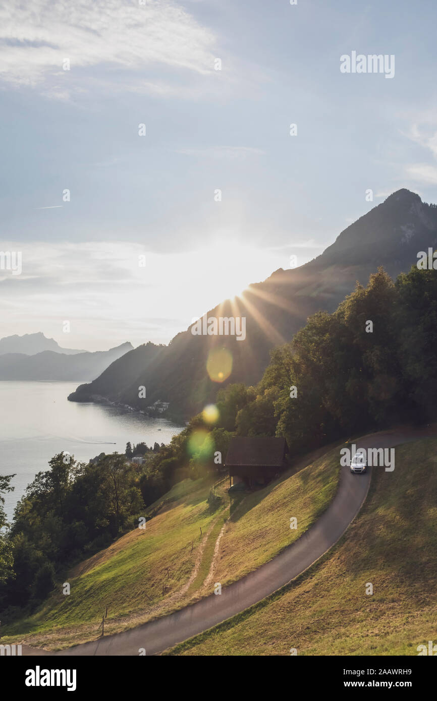 La Suisse, Lucerne, Schwyz, location de voiture sur route sinueuse au coucher du soleil avec le lac en arrière-plan Banque D'Images