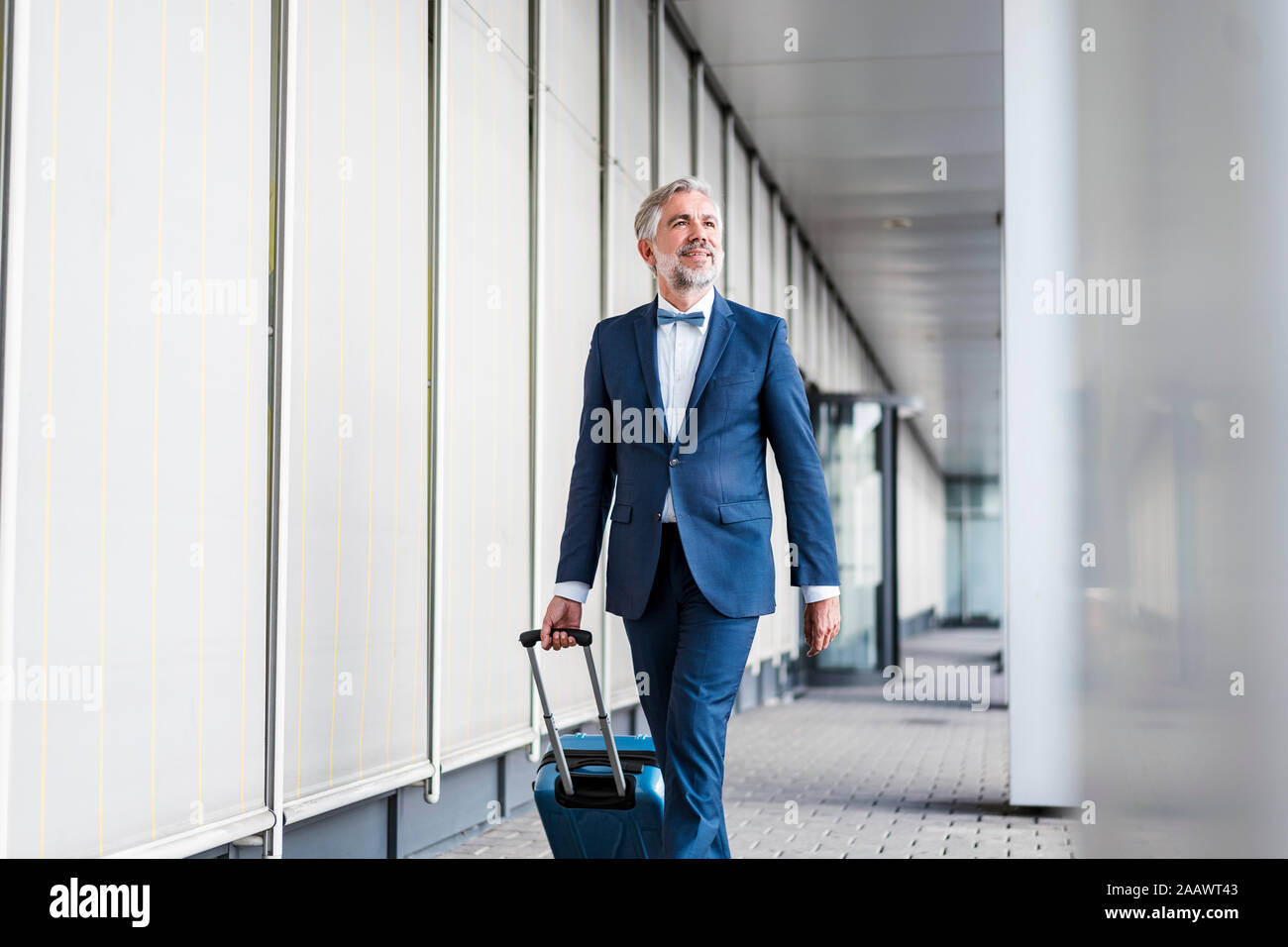 Mature businessman dans une zone de passage avec valise roulant sur le rendez-vous Banque D'Images