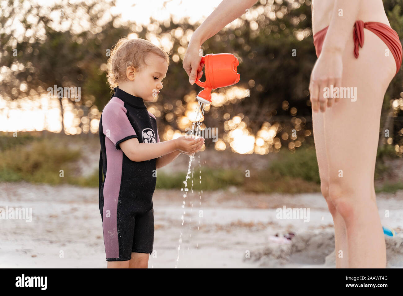 Mère verser de l'eau sur les mains de fille sur la plage Banque D'Images