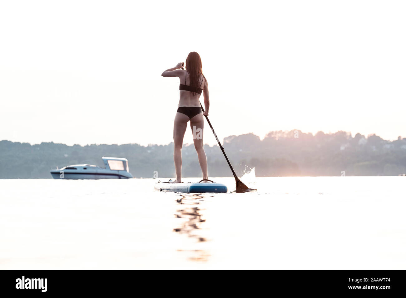 Vue arrière de jeune femme en stand up paddle à l'embarquement au coucher du soleil, le Lac de Starnberg, Allemagne Banque D'Images